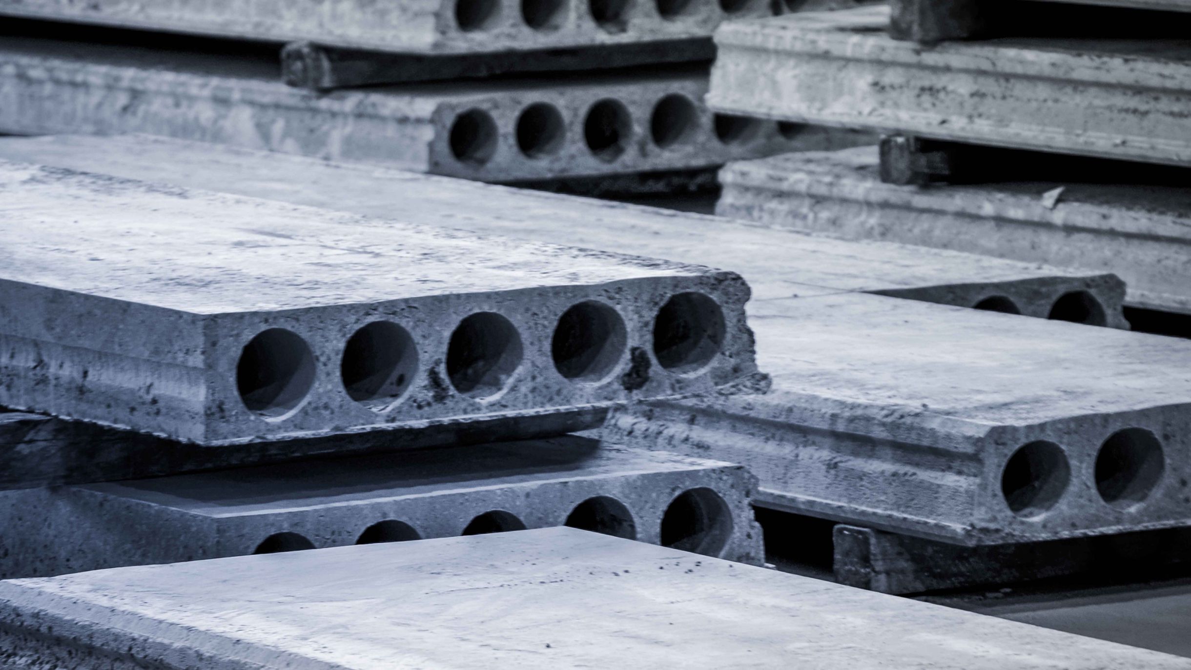 Stacked precast hollowcore slabs with round voids visible on the edges, stored in a concrete yard.