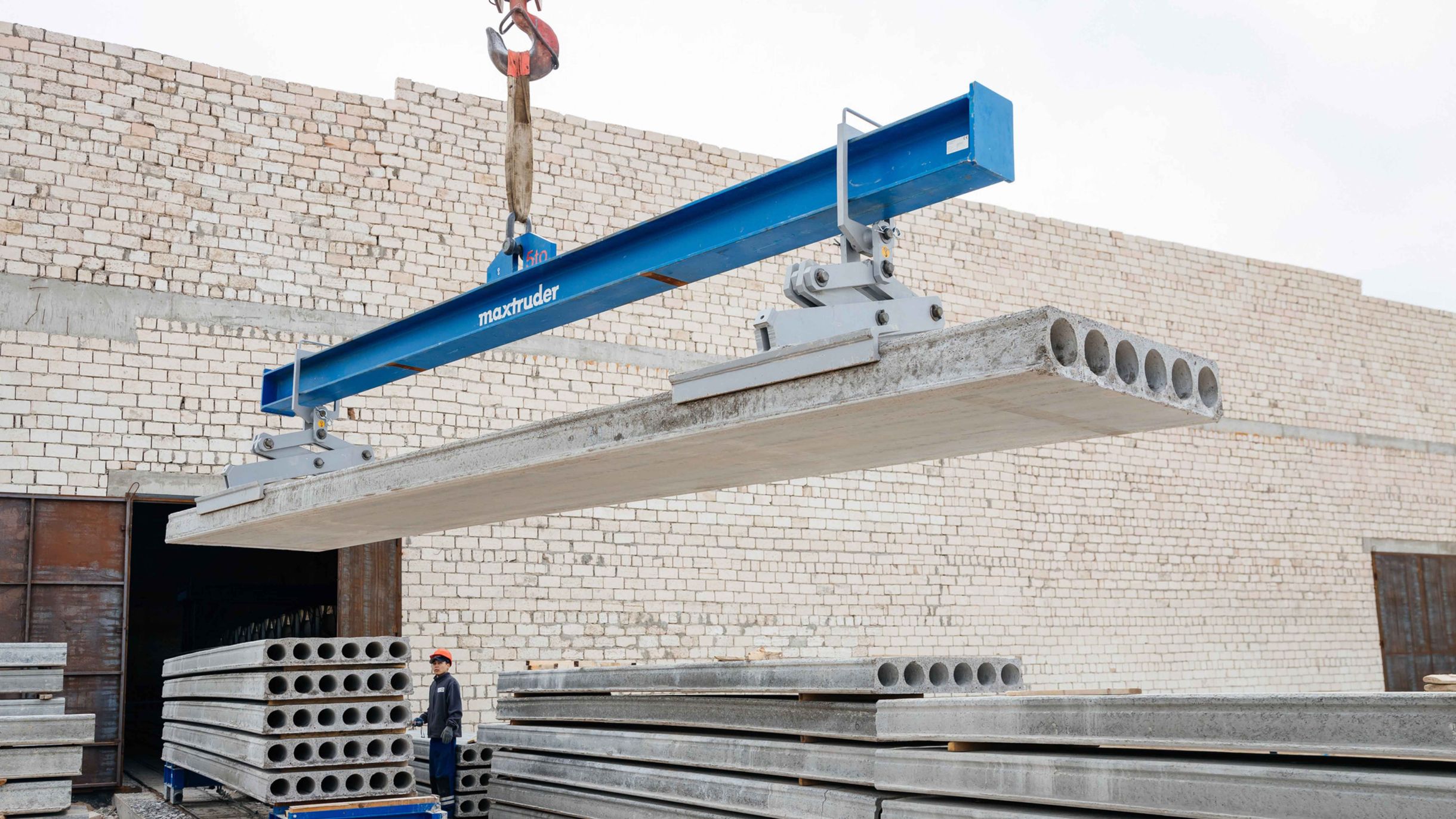 A hollowcore slab is being lifted by a crane using a lifting beam from the brand MAX-ruder.