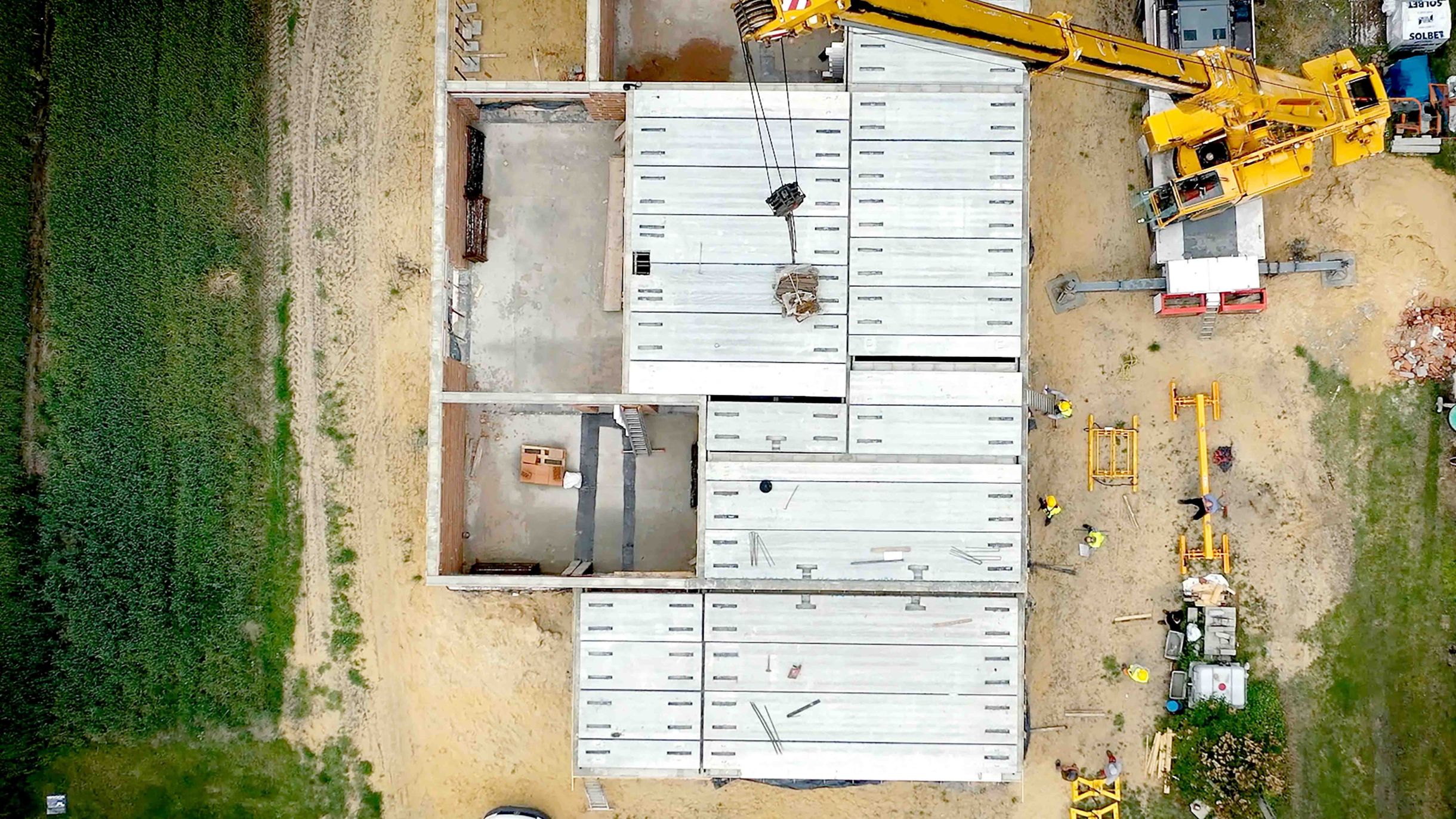 Aerial view of a construction site where hollow-core slabs are being installed. A yellow crane is positioning another slab.
