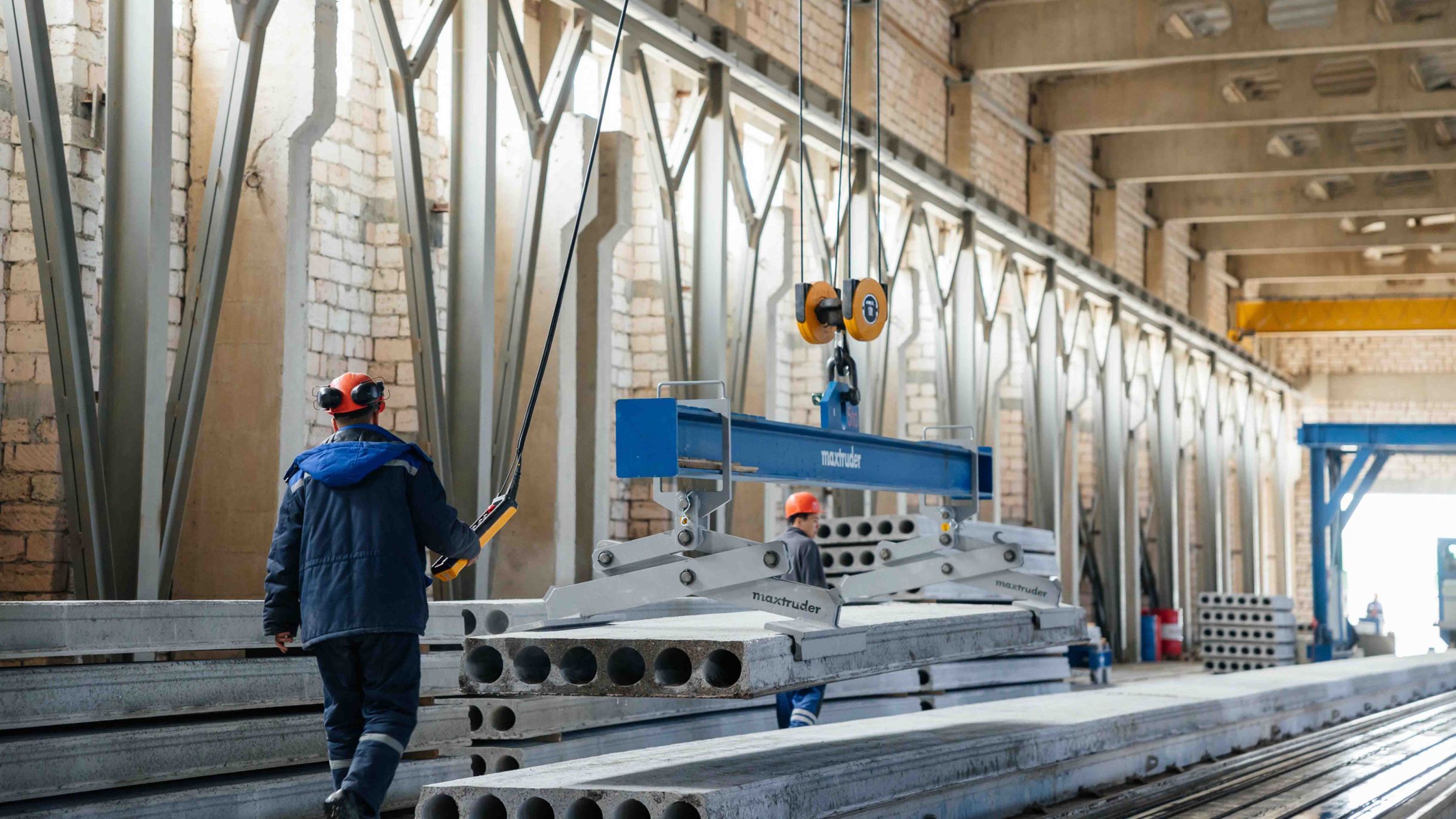Workers use a MAX-truder lifting system to move prestressed hollowcore slabs in the production hall.