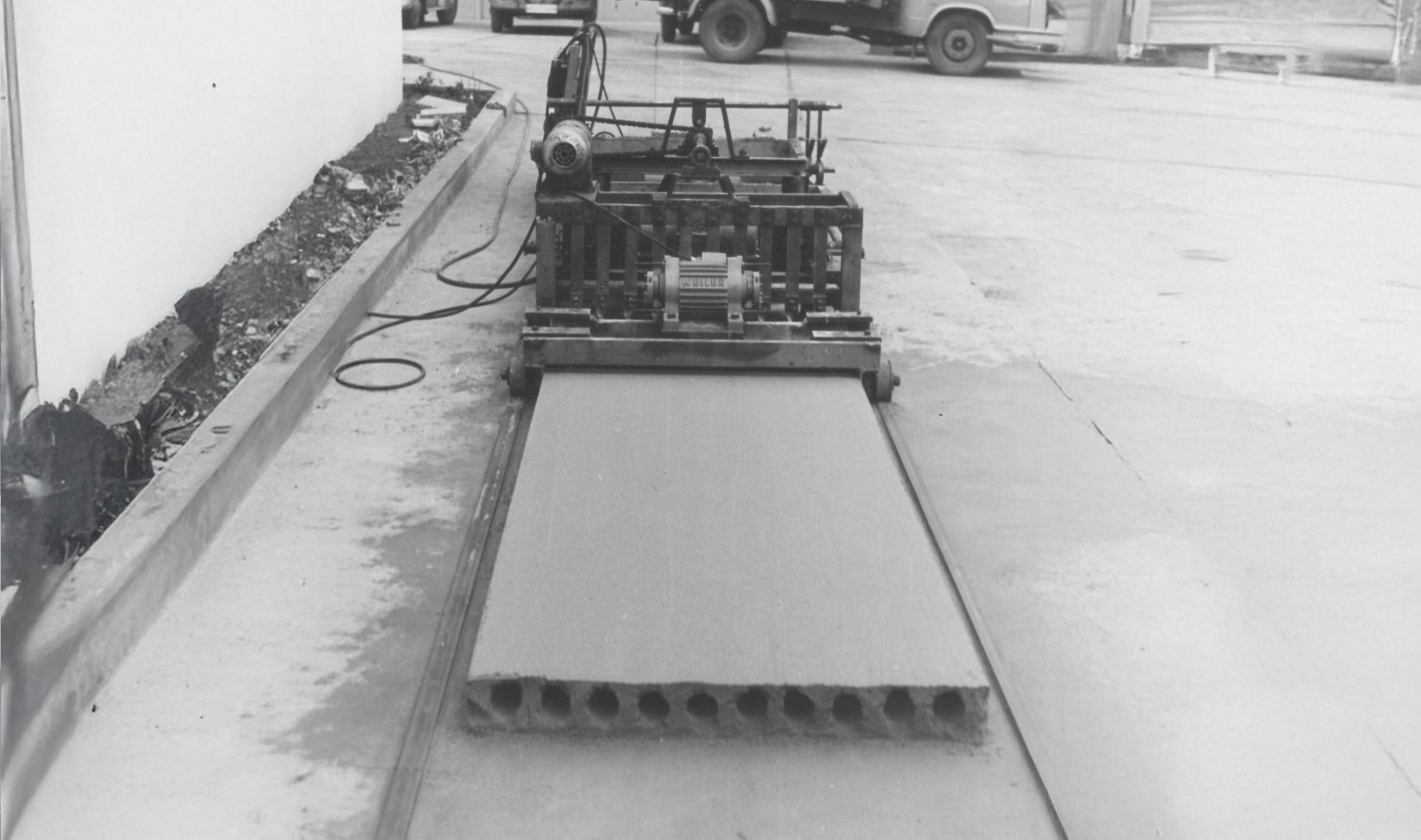 Black-and-white photo from 1964: a Weiler machine forms a hollowcore slab on the casting bed, round voids visible at the slab end.