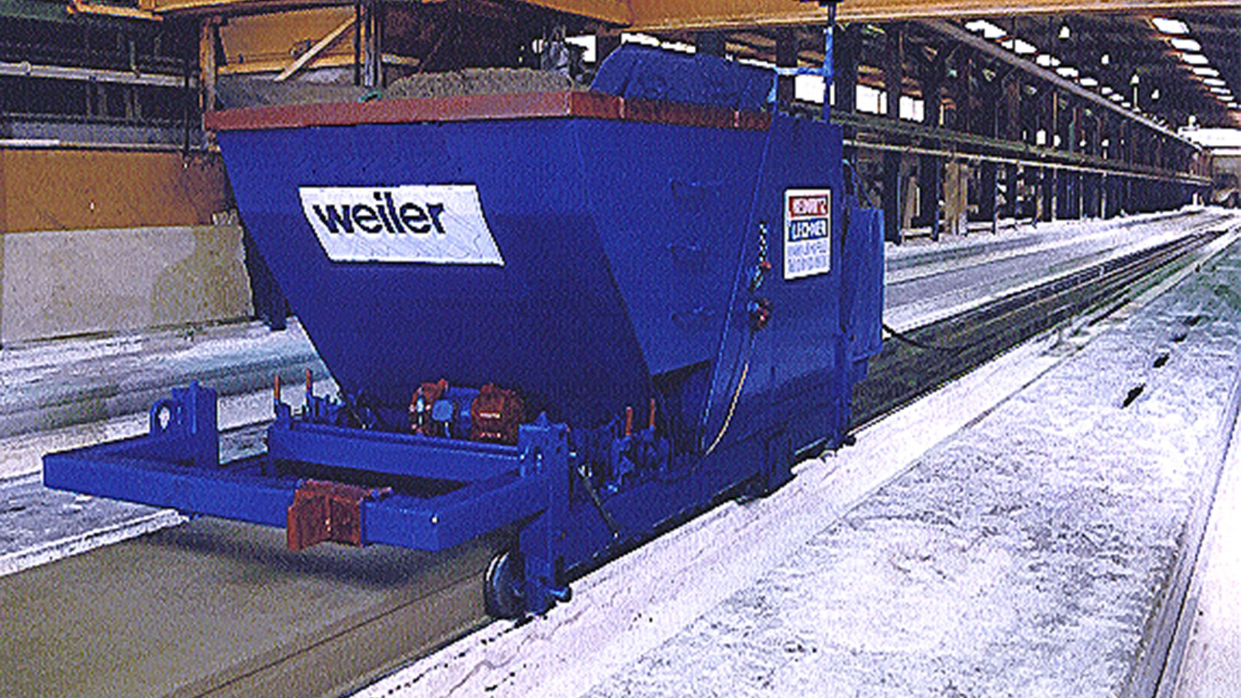 Colour photo from 1999: a blue Weiler machine runs on rails along a long casting bed inside a production hall.